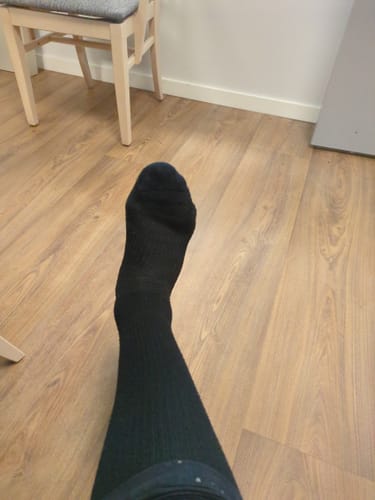 Customer's Diasocks Stödstrumpor, black knee-high compression sock worn on a leg against a wooden floor background.